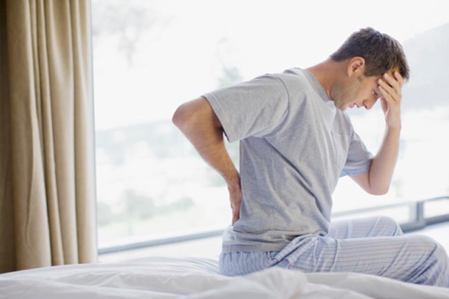 Man sitting on bed with backache and headache