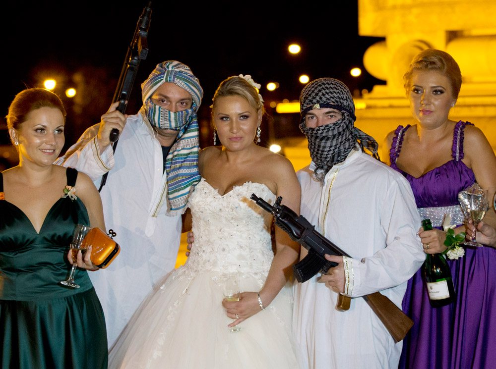 In this Sunday, Aug. 26, 2012 picture, a Romanian bride poses with mock kidnappers holding a toy weapons at the Triumph Arch in Bucharest, Romania. The arch, a replica of the Arc de Triomphe in Paris, the French capital, is a rendezvous place for brides on the wedding night for the bride stealing ritual. The ancient Romanian tradition of bride stealing is getting bigger, brasher and an increasingly common sight in the Romanian capital, the region's undisputed party town. (AP Photo/Vadim Ghirda)